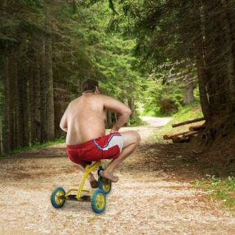 Adult naked man cycling on child’s bicycle