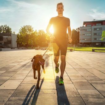 Silhouettes of runner and dog on city street under sunrise sky i